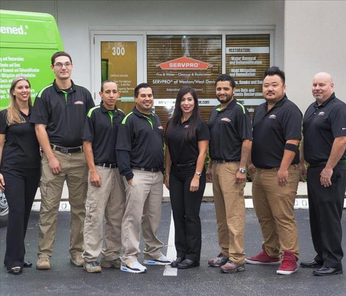 Team of people standing in between two green vans and infront of company building