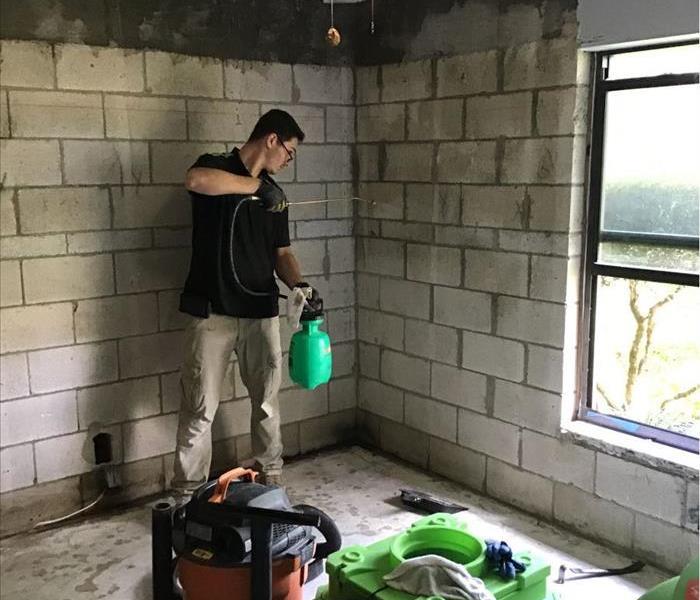 Man standing in the corner of the room spraying a chemical on a concrete wall