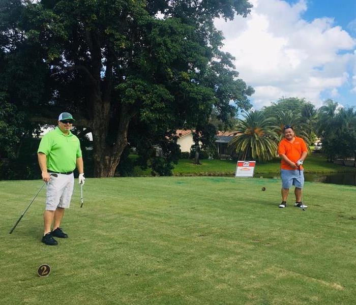 two men on a golf course one on right in an orange shirt, one on left in a green shirt