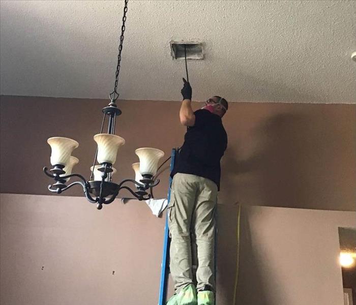 SERVPRO employee standing on a ladder to reach the duct work that needs a cleaning