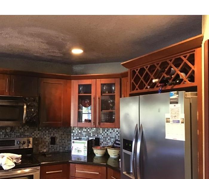 kitchen with medium brown cabinetry and stainless steel appliances has soot and smoke damage on ceiling and cabinents