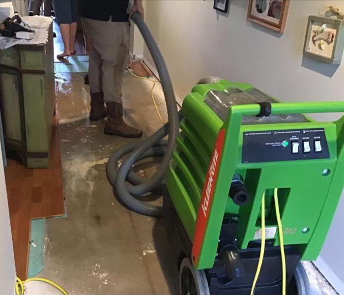hallway with part of wood flooring removed exposing concrete and a man using a water extraction tool to suck up water on floo